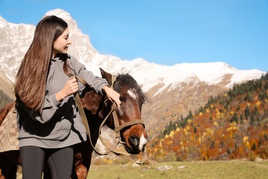 Photo of Young woman with horse in mountains on sunny day, space for text. Beautiful pet