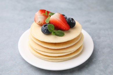 Stack of tasty pancakes with fresh berries and mint on light grey table, closeup