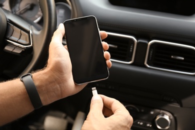 Photo of Man connecting charging cable to smartphone in car, closeup