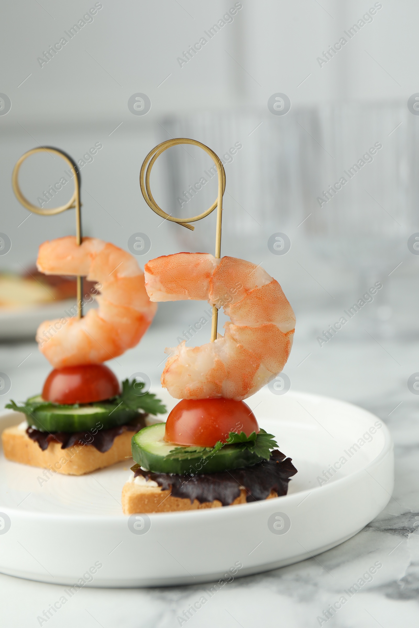 Photo of Tasty canapes with shrimps, cucumber, greens and tomatoes on white marble table