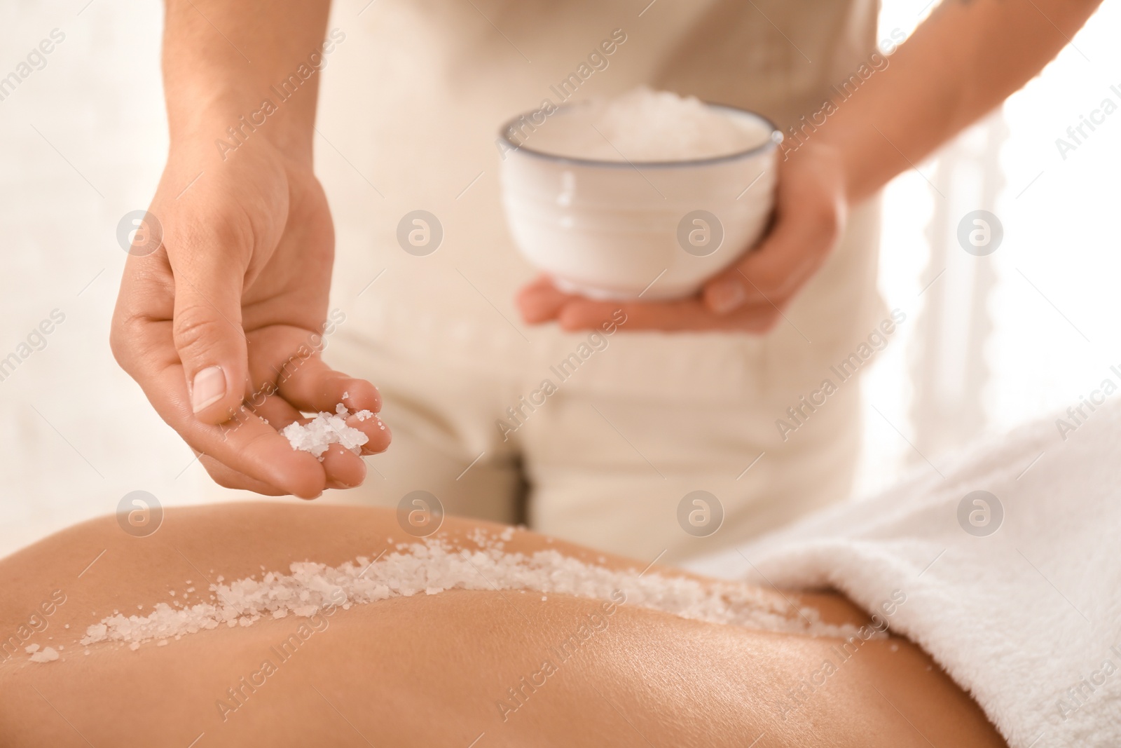 Photo of Young woman having body scrubbing procedure with sea salt in spa salon, closeup