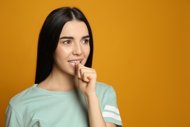 Photo of Young woman biting her nails on yellow background. Space for text