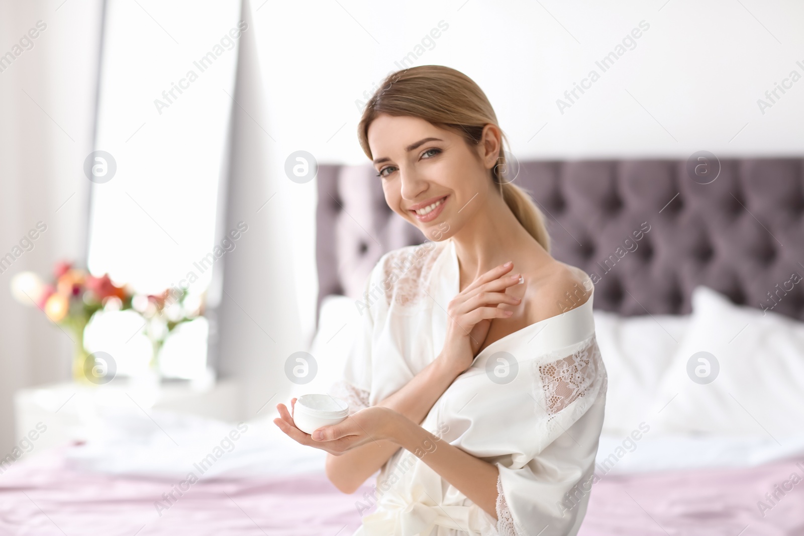 Photo of Young woman with jar of body cream at home