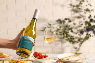 Photo of Woman holding bottle of wine over table with different snacks, closeup