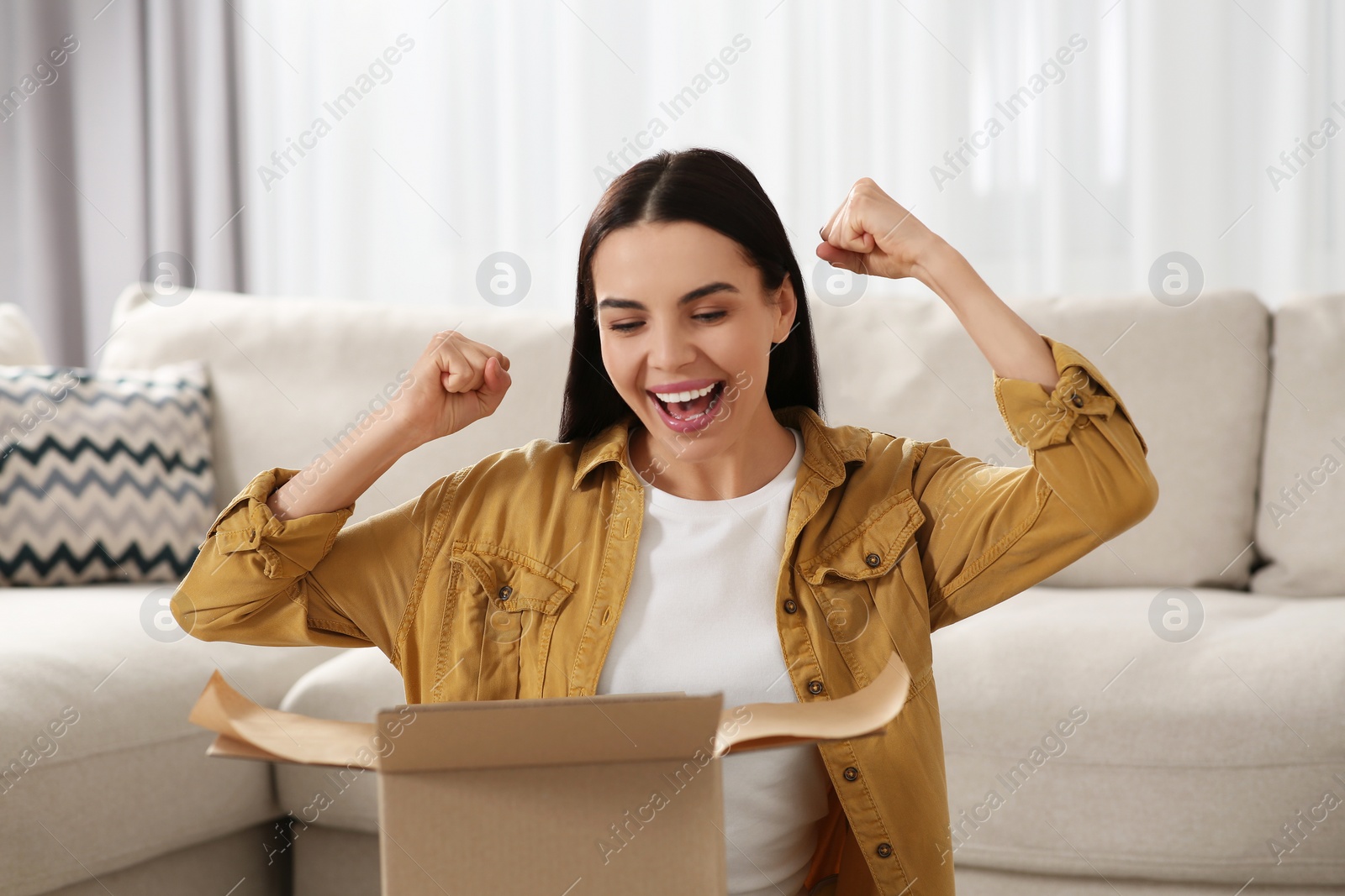 Photo of Emotional young woman opening parcel at home. Internet shopping