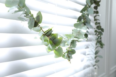 Photo of Beautiful garland made of eucalyptus branches hanging on window blinds indoors