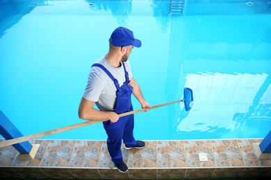 Male worker cleaning outdoor pool with scoop net