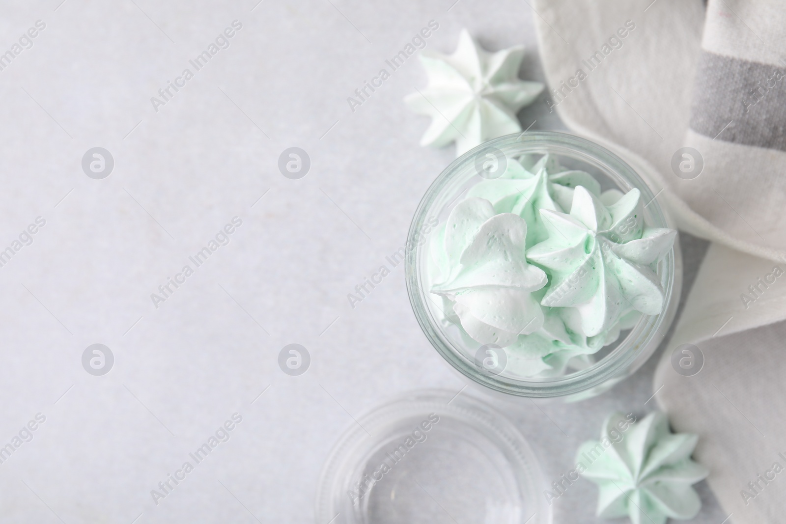 Photo of Tasty meringue cookies in glass jar on light grey table, top view. Space for text