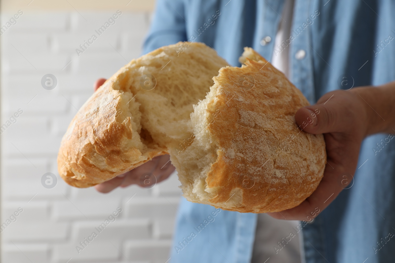 Photo of Man breaking loaf of fresh bread near white brick wall, closeup