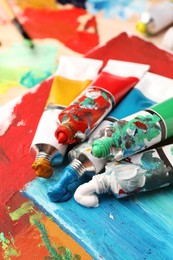 Photo of Tubes of colorful oil paints on canvas with abstract painting, closeup