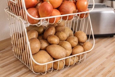 Photo of Container with potatoes and onions on wooden kitchen counter. Orderly storage