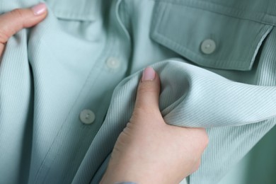 Photo of Woman touching shirt made of soft turquoise fabric, closeup