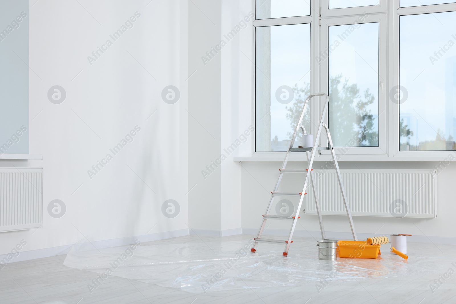 Photo of Stepladder and painting tools near window in empty room, space for text