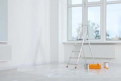 Photo of Stepladder and painting tools near window in empty room, space for text