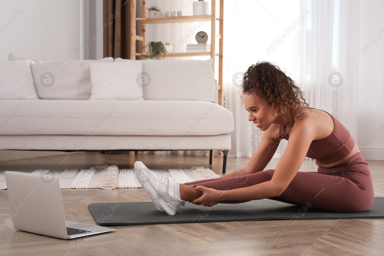 Photo of Beautiful African American woman stretching on yoga mat while watching online class at home