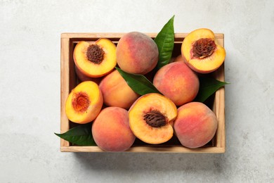 Photo of Delicious juicy peaches and leaves in crate on light grey textured table, top view