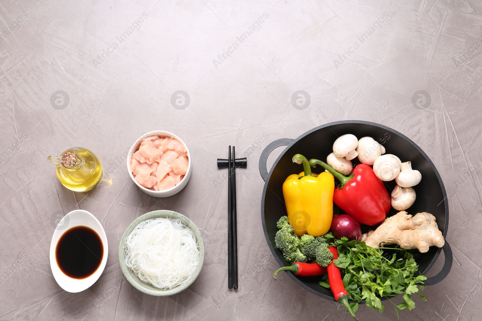 Photo of Wok, chopsticks and different products on grey textured table, flat lay. Space for text