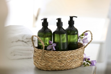 Photo of Wicker basket with soap dispensers , flowers and clean towels on table