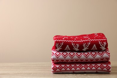 Stack of different Christmas sweaters on wooden table against beige background, space for text