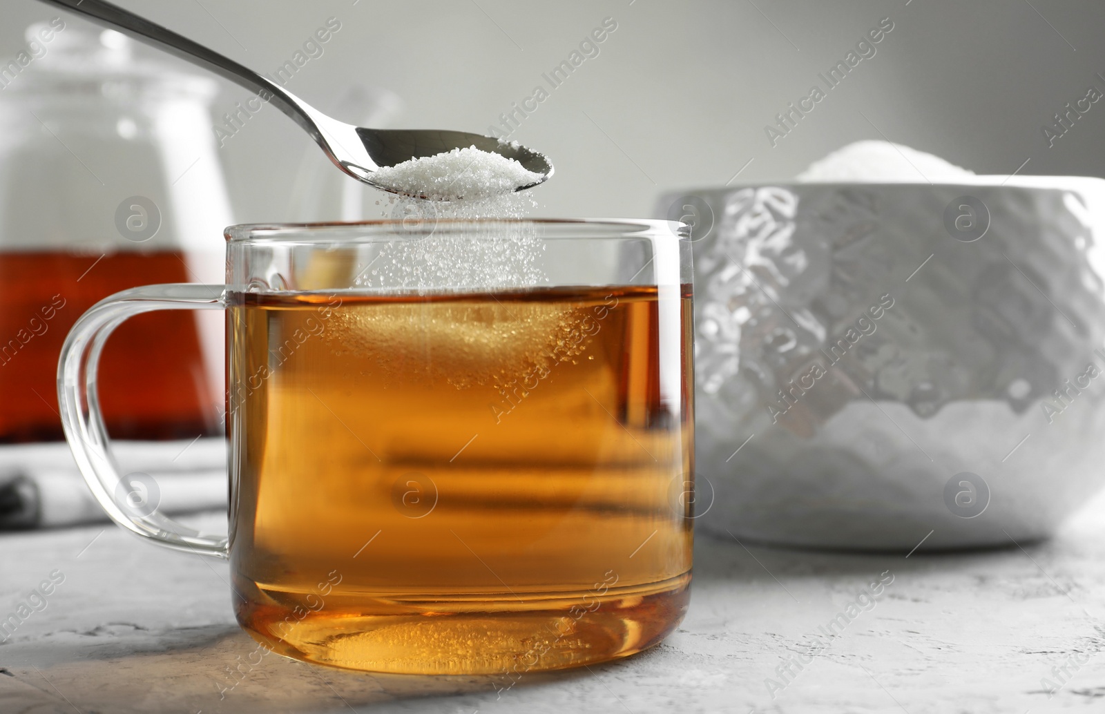 Photo of Adding sugar into cup of tea at grey textured table, closeup