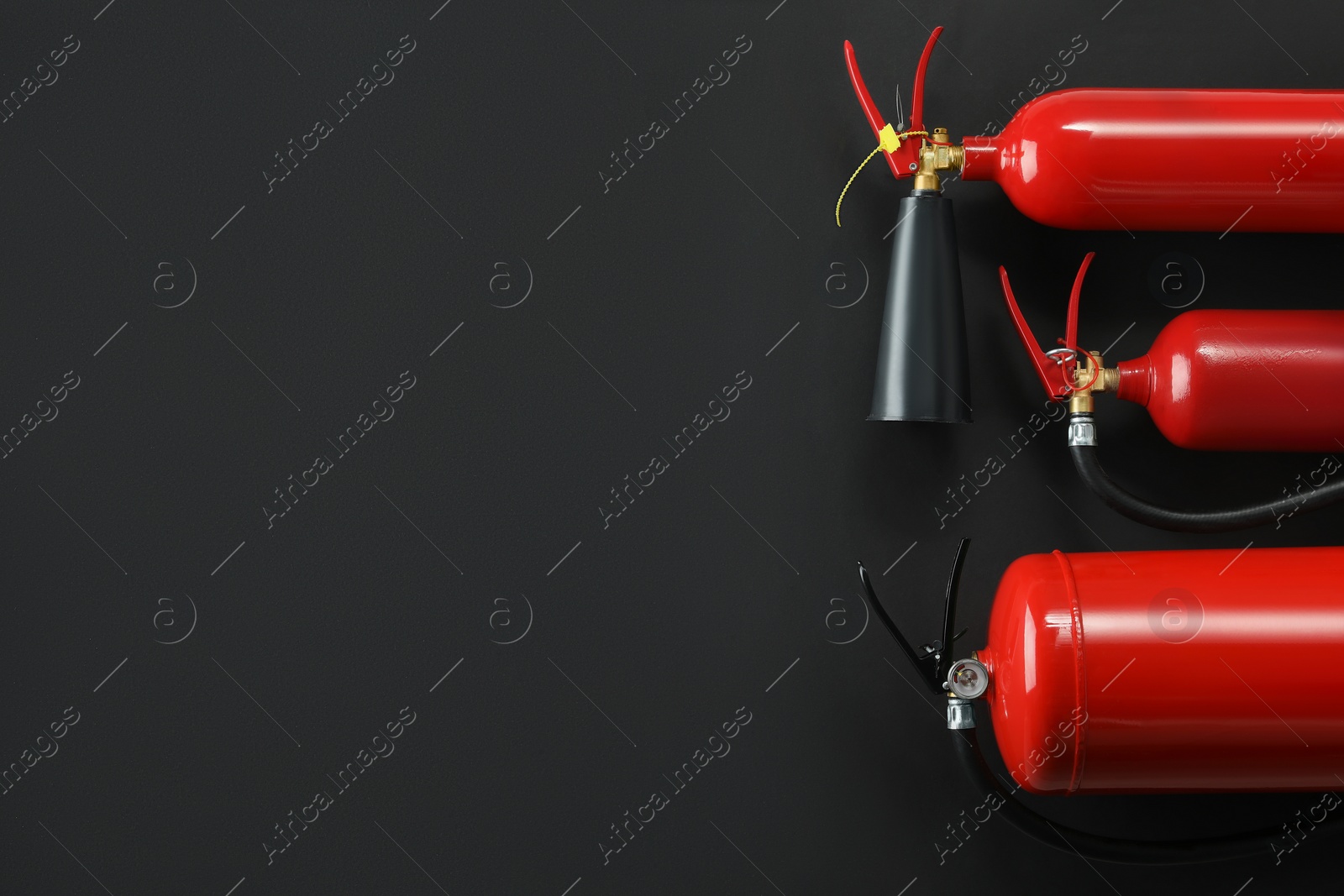 Photo of Different fire extinguishers on black background, flat lay. Space for text