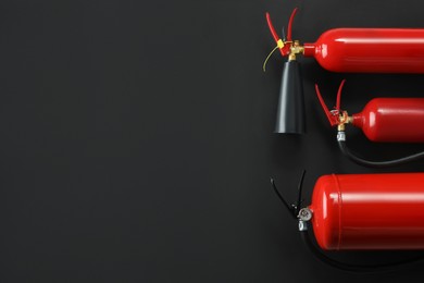 Photo of Different fire extinguishers on black background, flat lay. Space for text