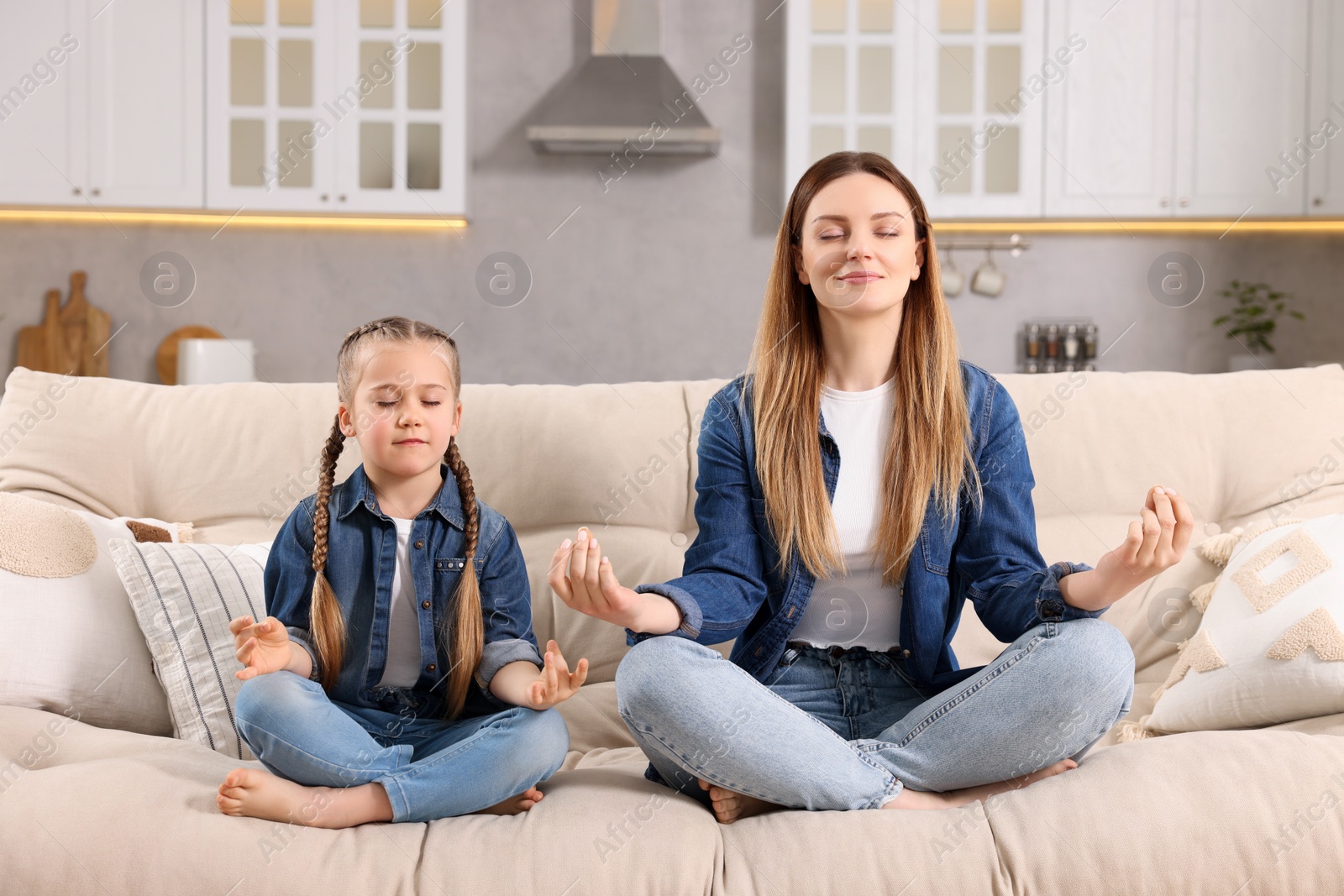 Photo of Mother with daughter meditating on sofa at home. Harmony and zen