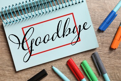 Image of Notebook with word Goodbye and markers on wooden table, flat lay