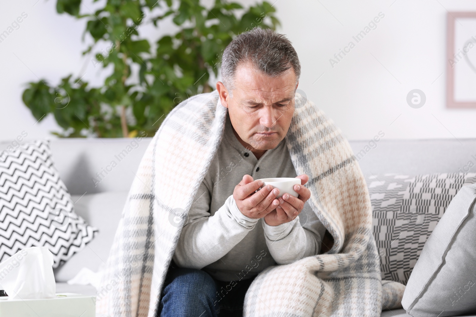 Photo of Man with cup of tea for cough on sofa at home