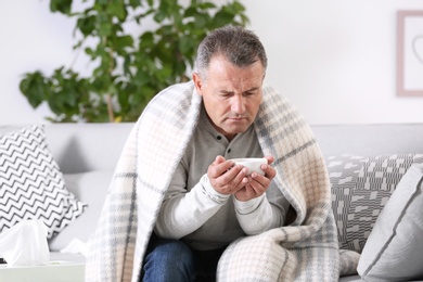 Man with cup of tea for cough on sofa at home