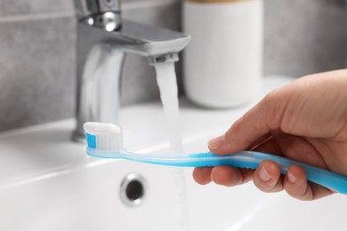 Woman holding plastic toothbrush with paste near flowing water above sink in bathroom, closeup