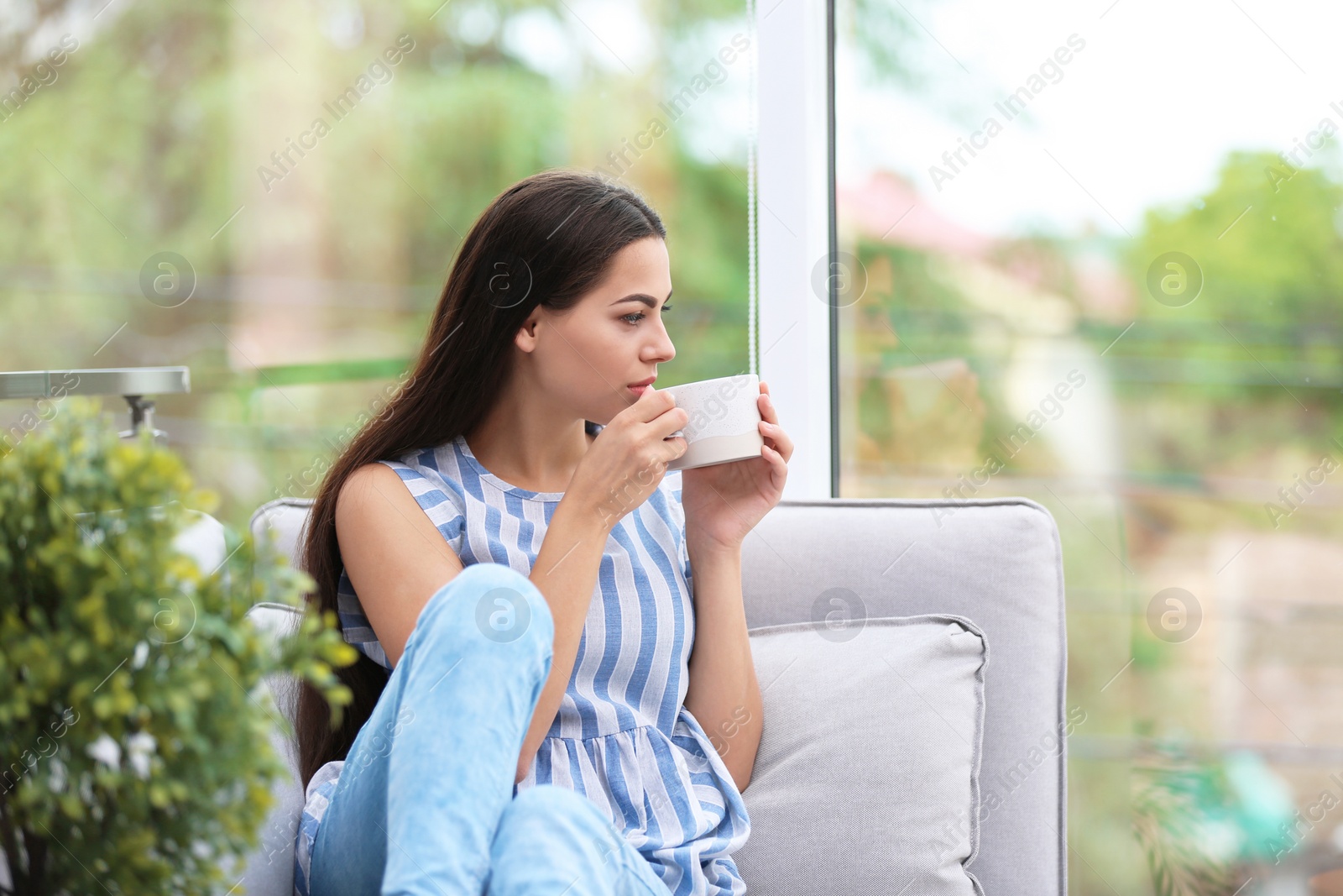 Photo of Young beautiful woman drinking morning coffee near window at home