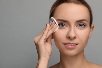 Photo of Beautiful woman removing makeup with cotton pad on grey background, closeup. Space for text