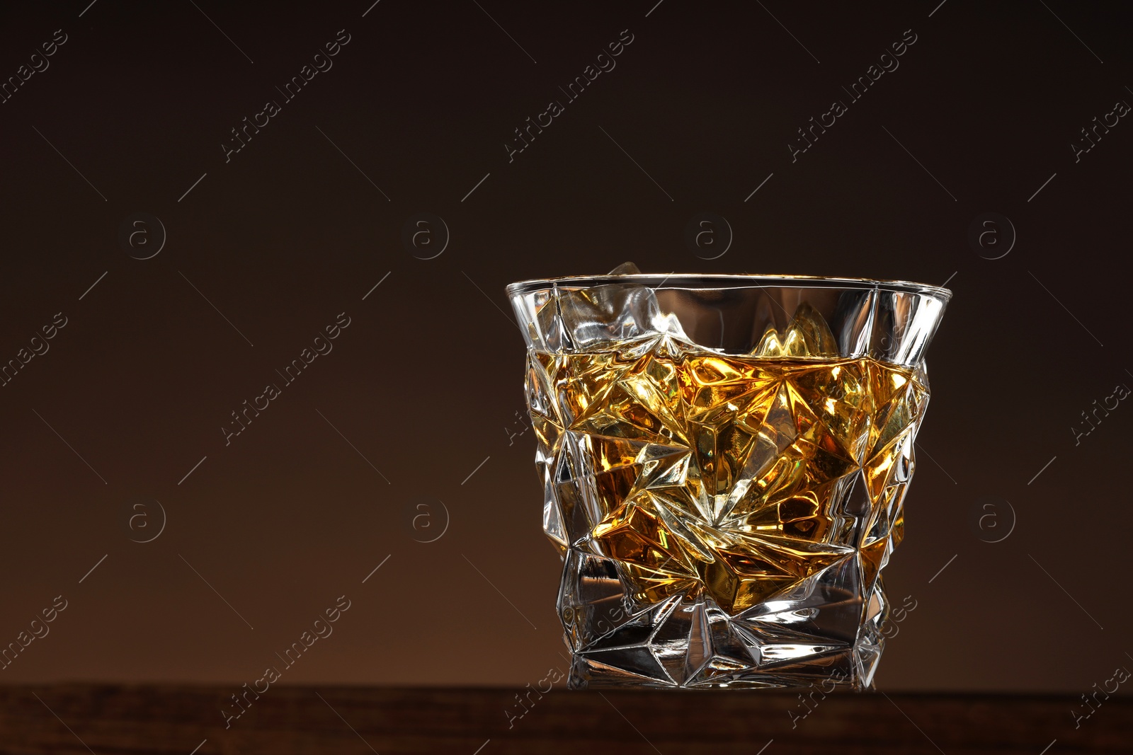 Photo of Whiskey with ice cubes in glass on table, closeup. Space for text