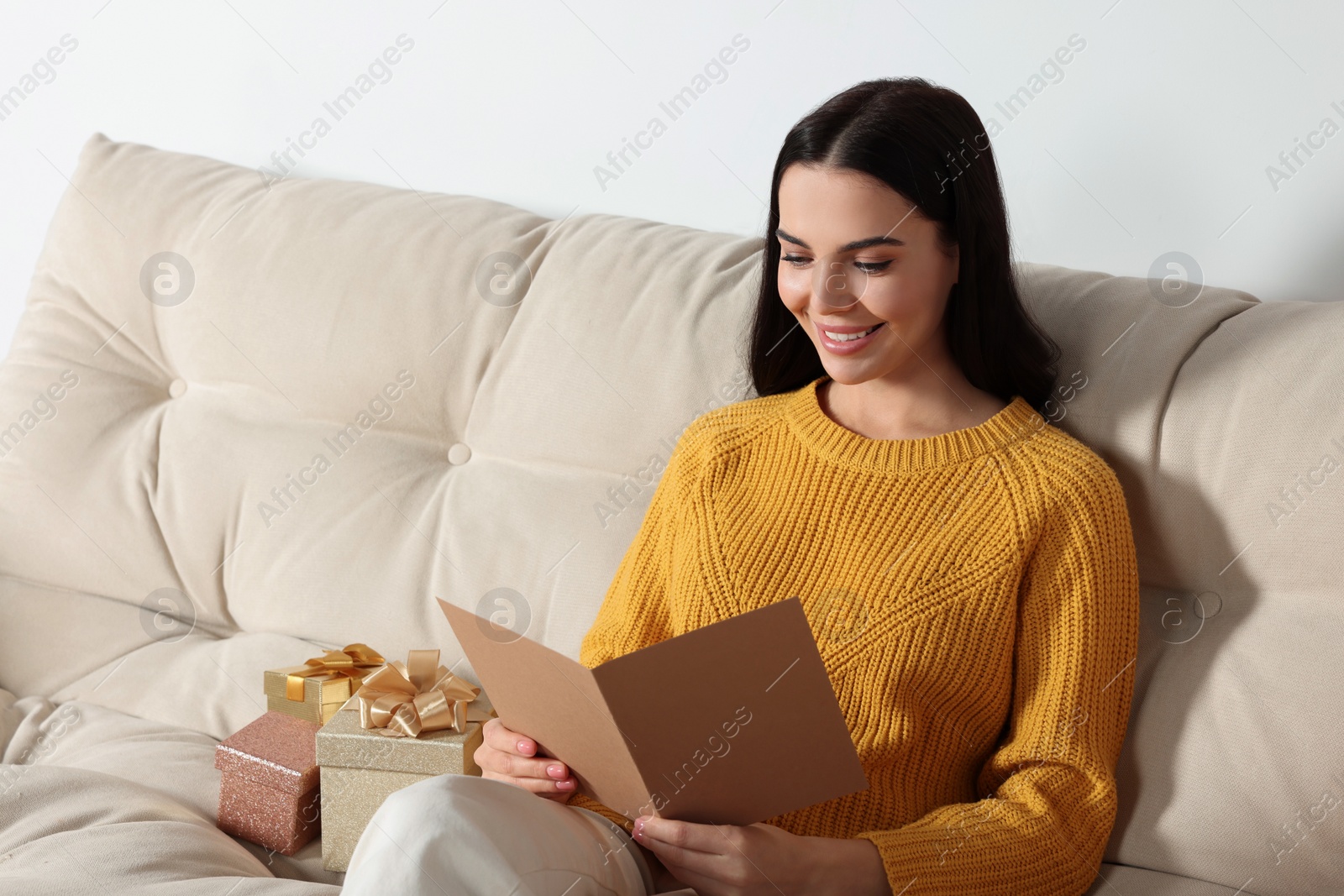 Photo of Happy woman reading greeting card on sofa in living room