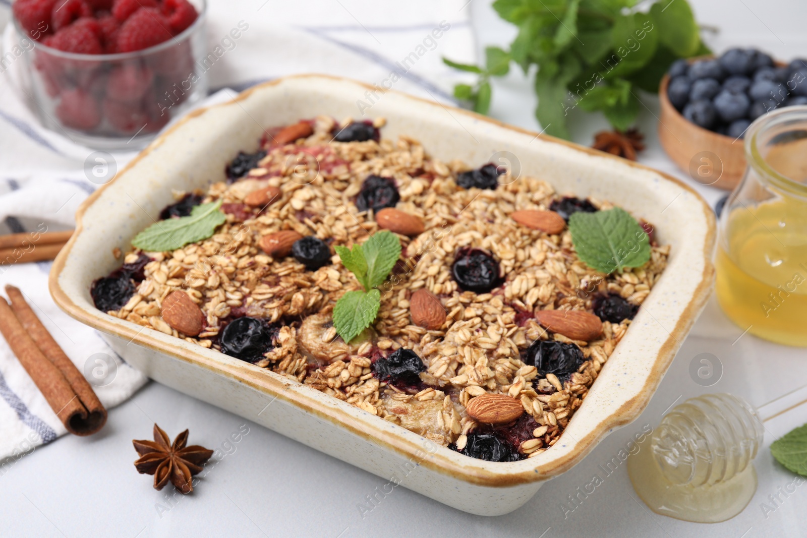 Photo of Tasty baked oatmeal with berries, almonds and spices in baking tray on white table, closeup