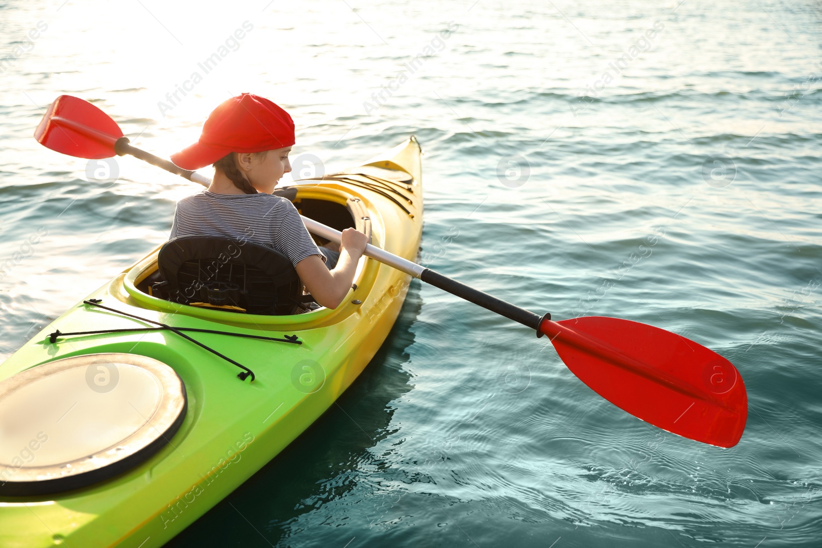 Photo of Little girl kayaking on river, back view. Summer camp activity