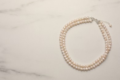 Beautiful pearl necklace on white marble table, top view. Space for text