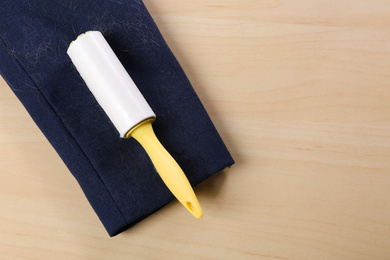 Photo of Lint roller and sleeve of jacket covered with hair on wooden table, flat lay. Space for text