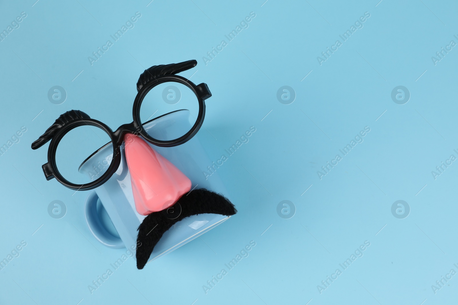 Photo of Man's face made of cup, fake mustache, nose and glasses on light blue background, top view. Space for text