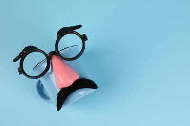 Man's face made of cup, fake mustache, nose and glasses on light blue background, top view. Space for text