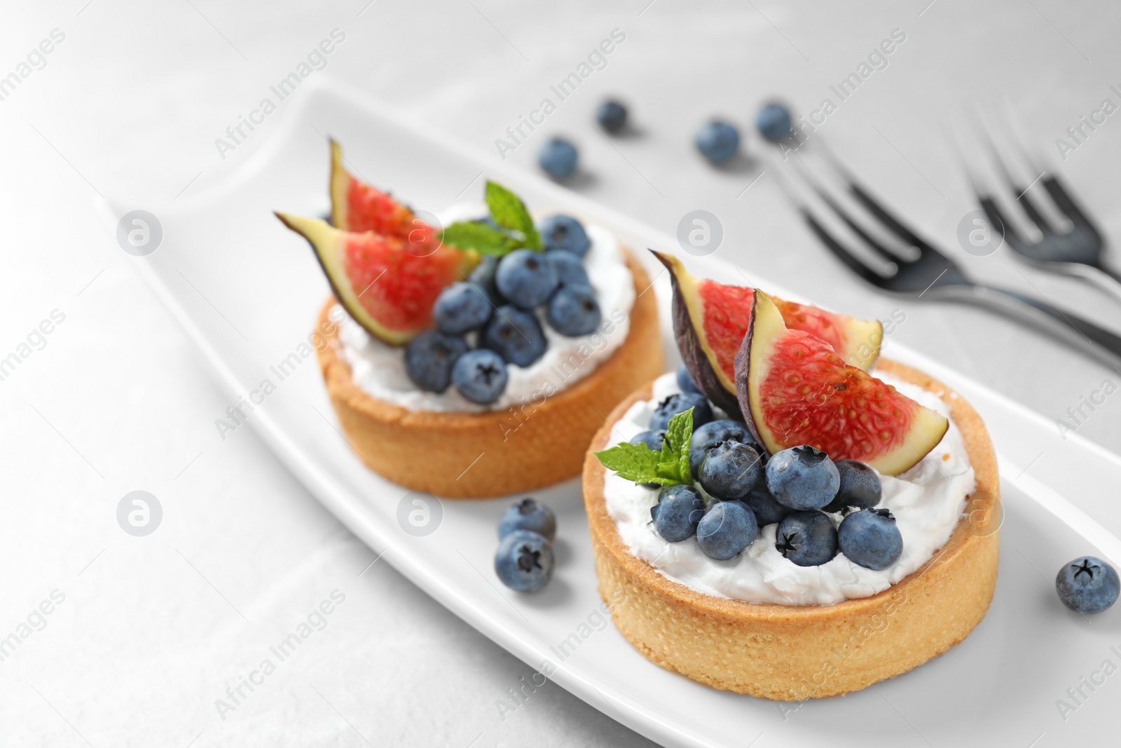 Photo of Tarts with blueberries and figs served on light table. Delicious pastries