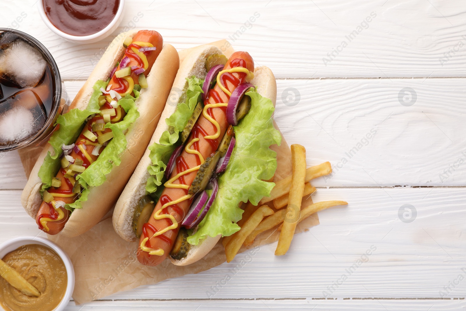 Photo of Delicious hot dogs with lettuce, onion and pickle served on white wooden table, flat lay. Space for text