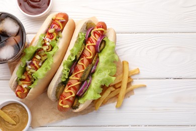 Delicious hot dogs with lettuce, onion and pickle served on white wooden table, flat lay. Space for text