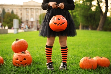 Photo of Little girl with pumpkin candy bucket wearing Halloween costume in park, closeup