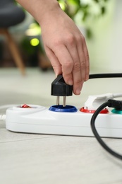 Photo of Woman inserting power plug into extension cord on floor indoors, closeup. Electrician's professional equipment