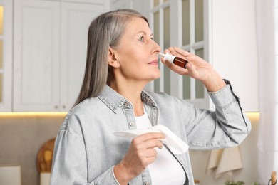 Photo of Medical drops. Woman with tissue using nasal spray indoors