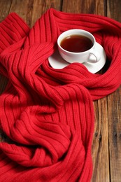 Photo of Red knitted scarf and tea on wooden table