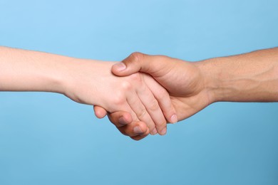 Photo of International relationships. People holding hands on light blue background, closeup