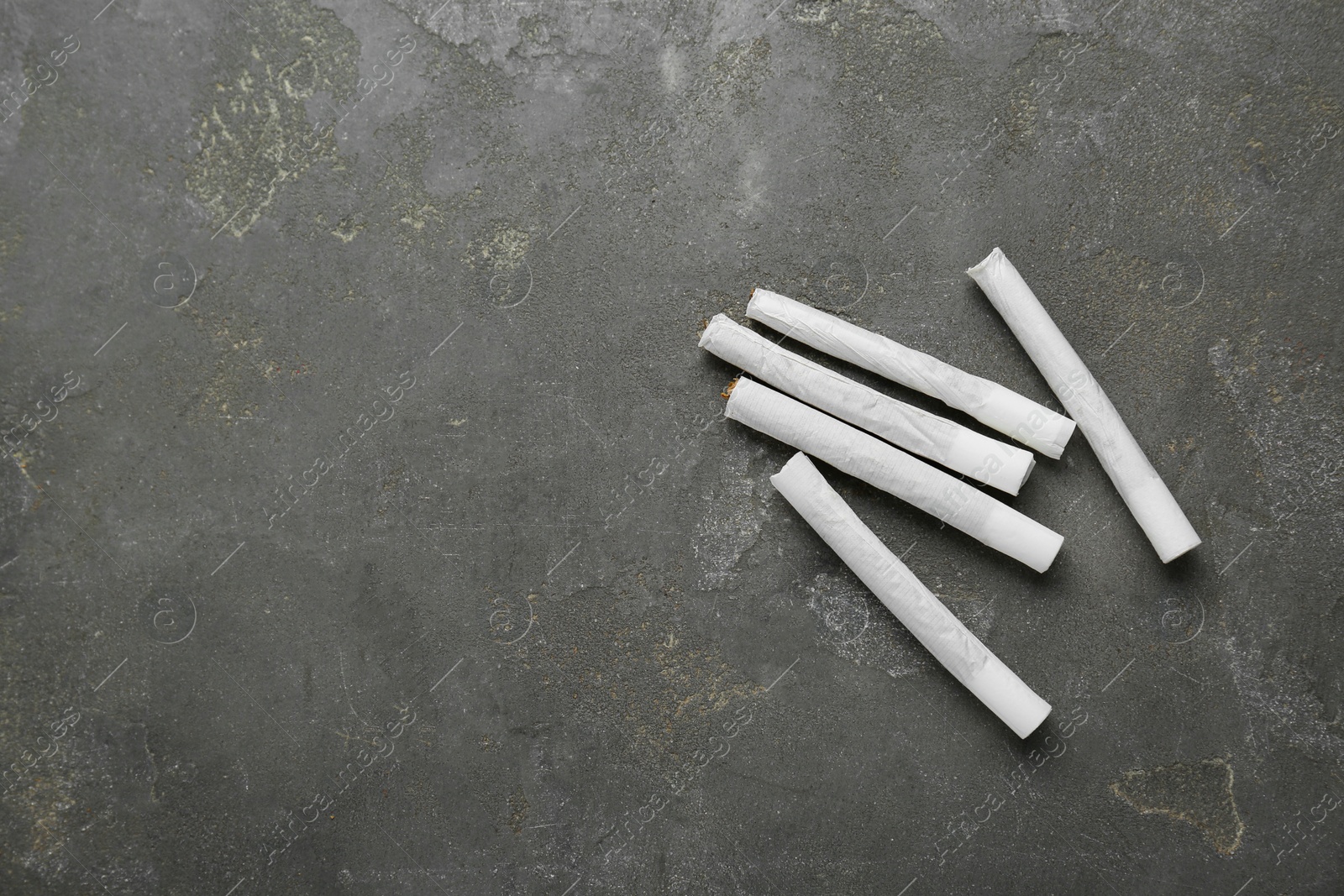 Photo of Hand rolled cigarettes with tobacco on dark grey background, flat lay. Space for text